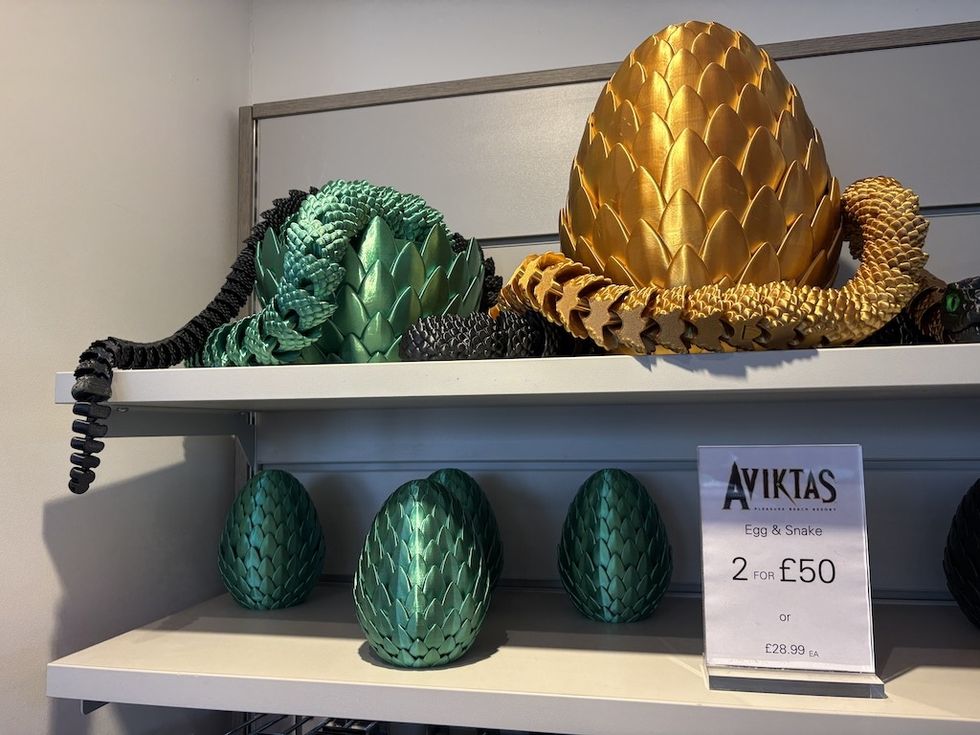 Gold and green dragon eggs with coiled snakes on display shelf.