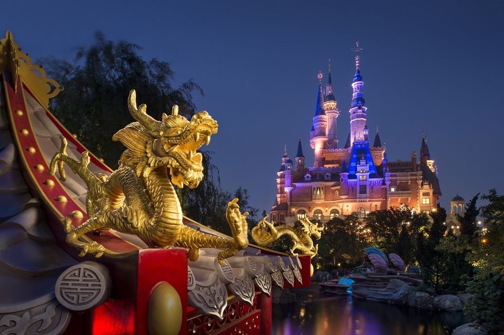 Golden dragon statue with illuminated Disney castle backdrop at night.
