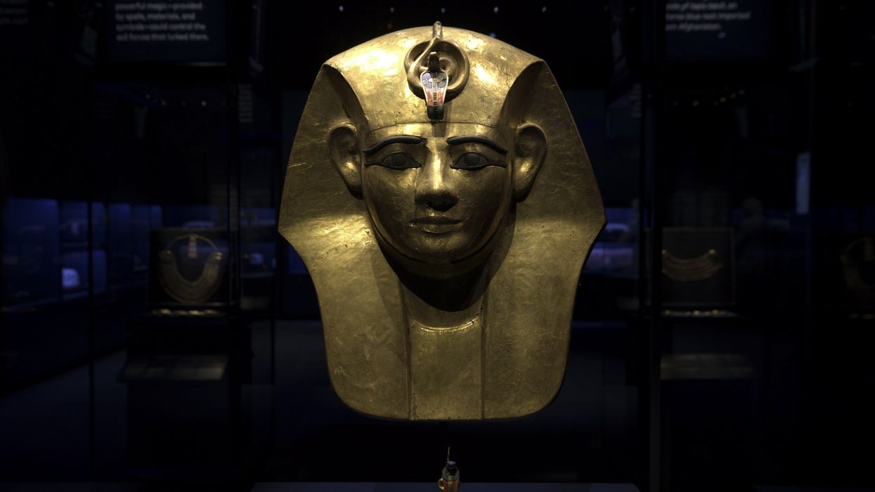 Golden Egyptian mask displayed in a dimly lit museum setting.