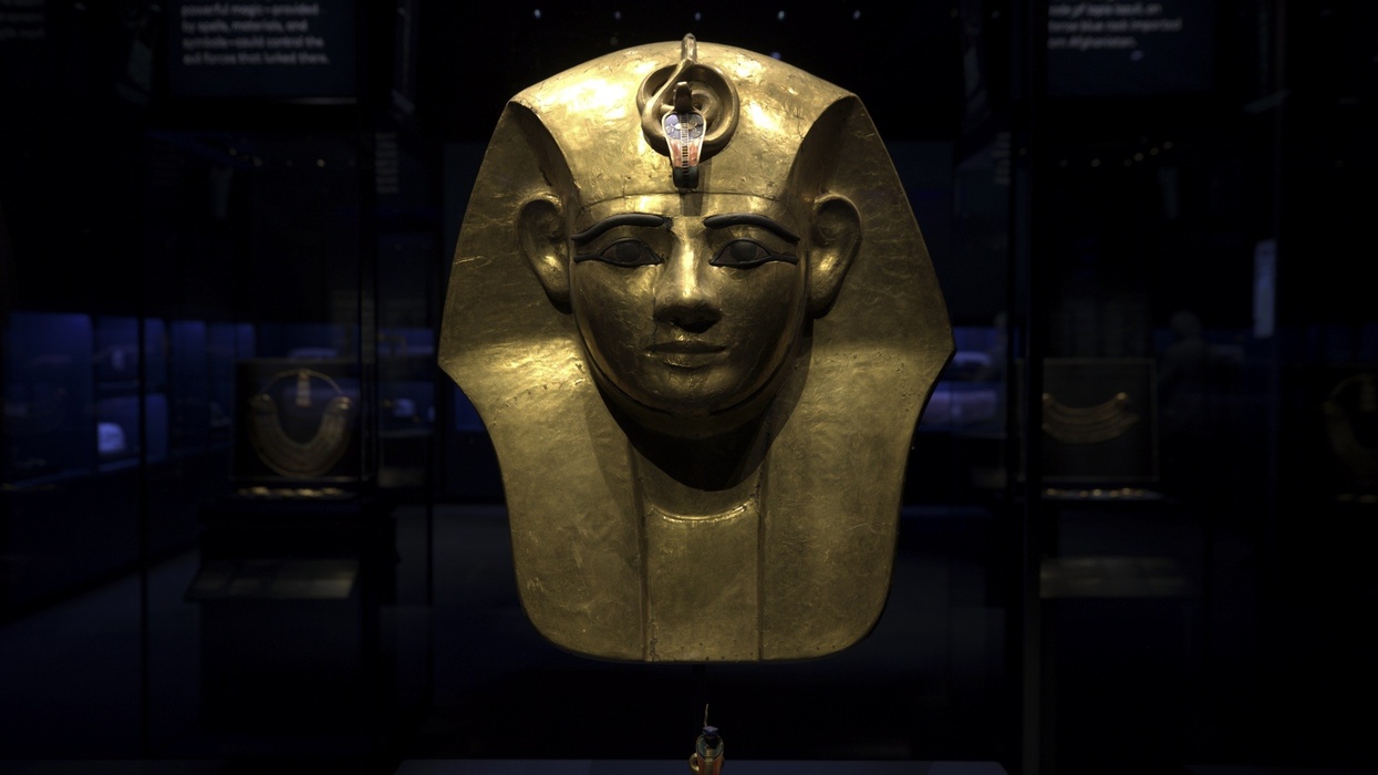 Golden Egyptian mask displayed in a dimly lit museum setting.