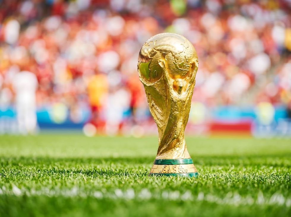 Golden football trophy on grass, colorful blurred crowd in background.