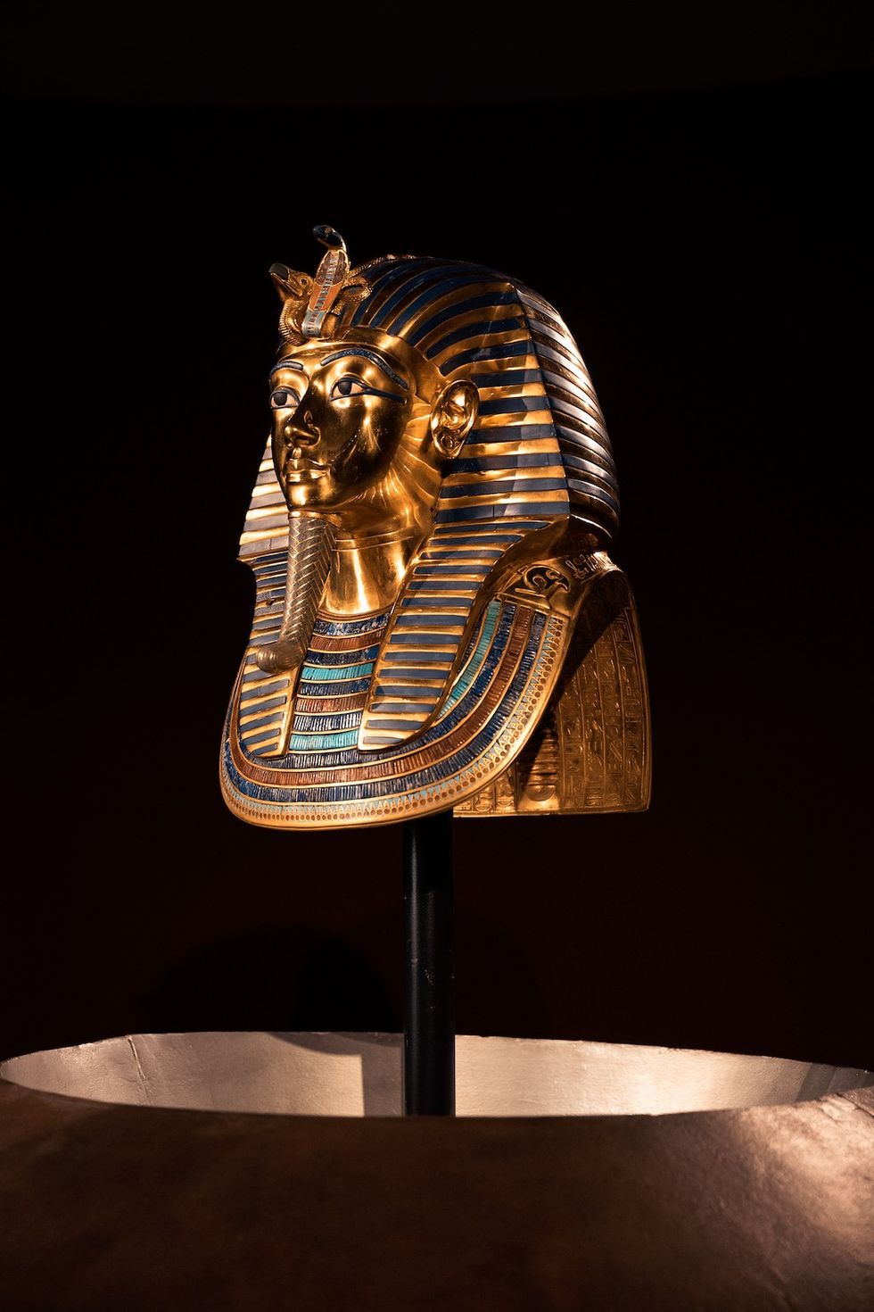 Golden pharaoh's mask with blue stripes on display in dim lighting.