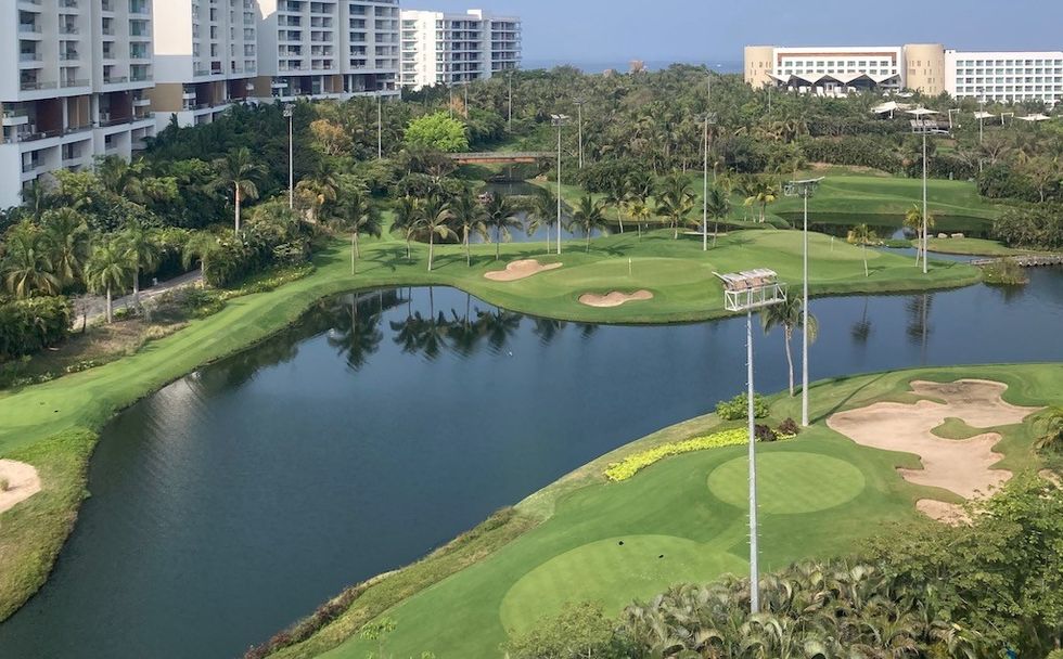 Golf course with ponds, sand traps, palm trees, and nearby high-rise buildings.