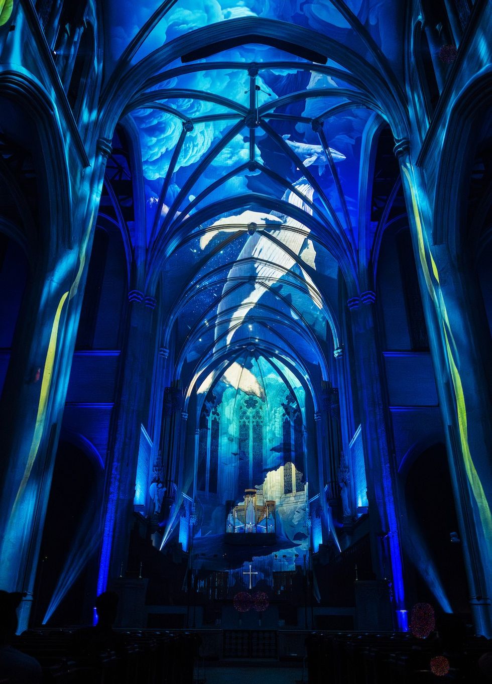 Gothic church interior illuminated by vibrant blue light projections of marine scenes.