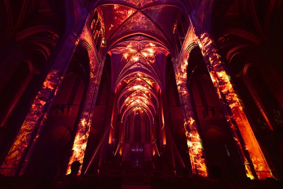 Gothic church interior illuminated with vibrant red and orange lighting projections.