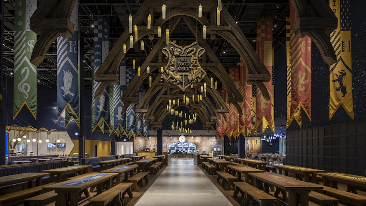 Gothic hall with long tables, floating candles, and colorful banners hung from wooden beams.