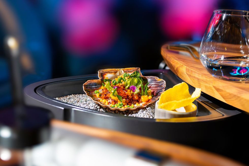 Gourmet seafood dish in a shell, served on pebbles with a glass on a wooden tray at Eatrenalin.