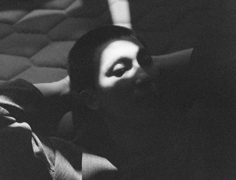 Grainy black and white photo of BTS' RM resting with eyes closed, shadow across face.