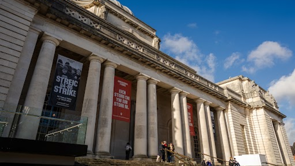Grand building with tall columns and people on steps, under a blue sky.