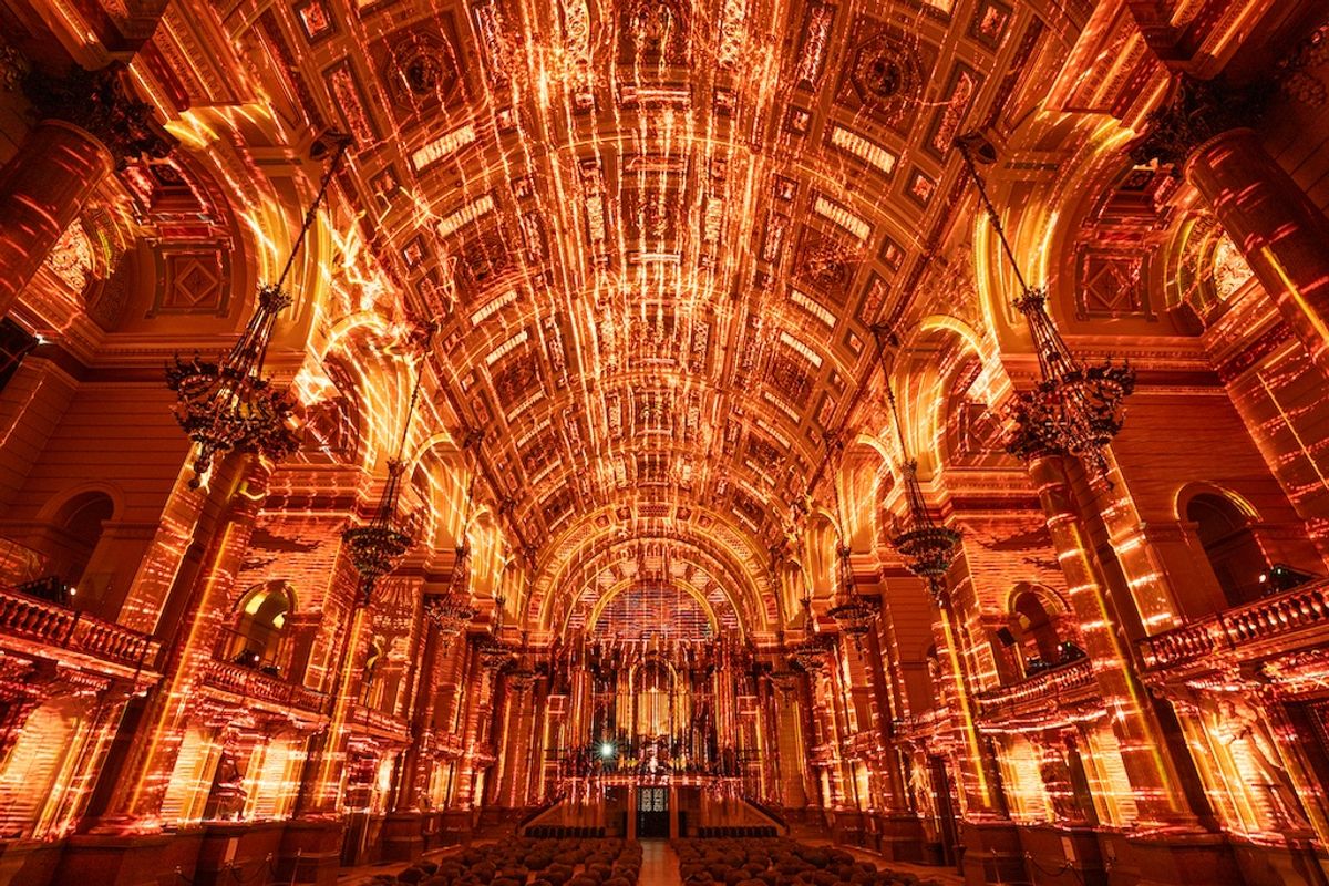 Grand hall with luminous, intricate orange and gold light patterns on ceiling and arches.