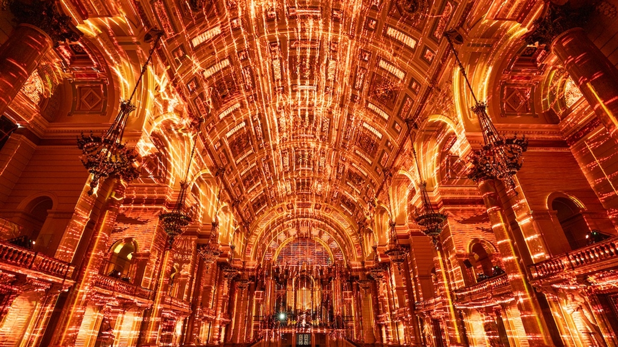 Grand hall with luminous, intricate orange and gold light patterns on ceiling and arches.