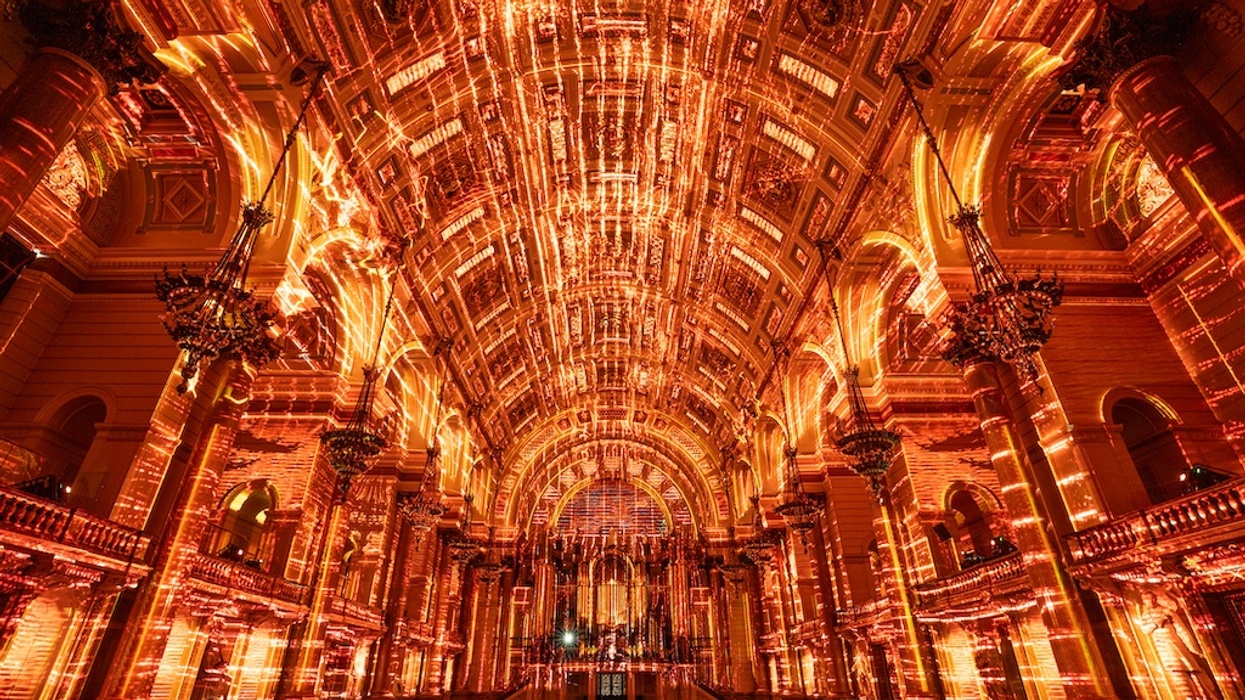 Grand hall with luminous, intricate orange and gold light patterns on ceiling and arches.