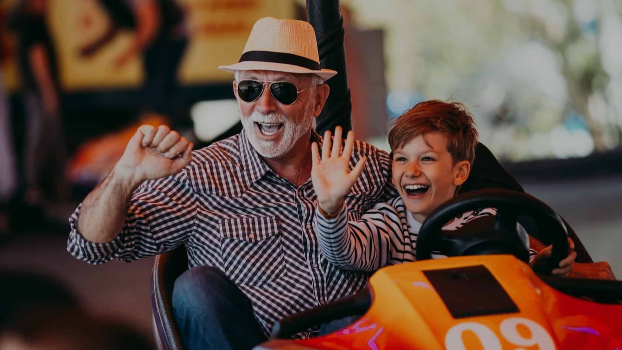 Grandfather and grandson having fun and spending good quality time together in amusement park. They enjoying and smiling while driving bumper car together.