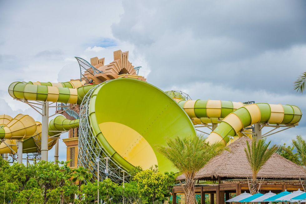 Green and yellow water slide at an outdoor water park, Aquaventure Waterpark in Sanya, with cloudy skies.