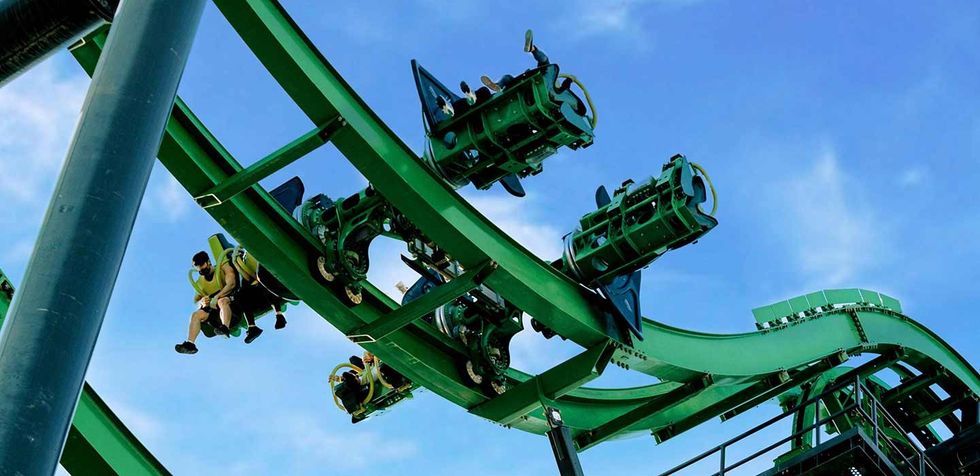 Green roller coaster with riders against a clear blue sky at Motiongate Dubai