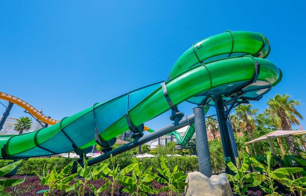 Green water slide spirals through lush park under clear blue sky at Land of Legends in Turkey