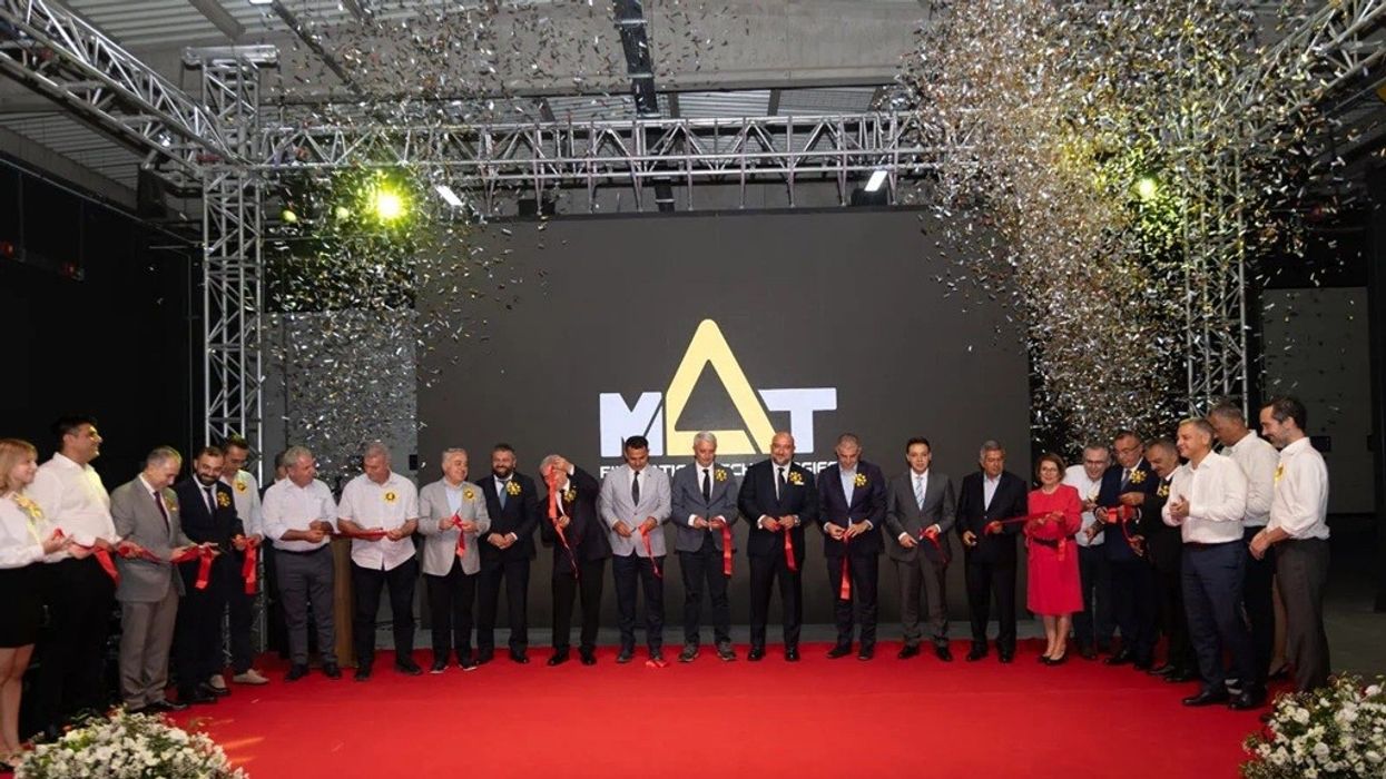 Group at ribbon-cutting ceremony on stage, confetti falling, large "MAT" logo in background.