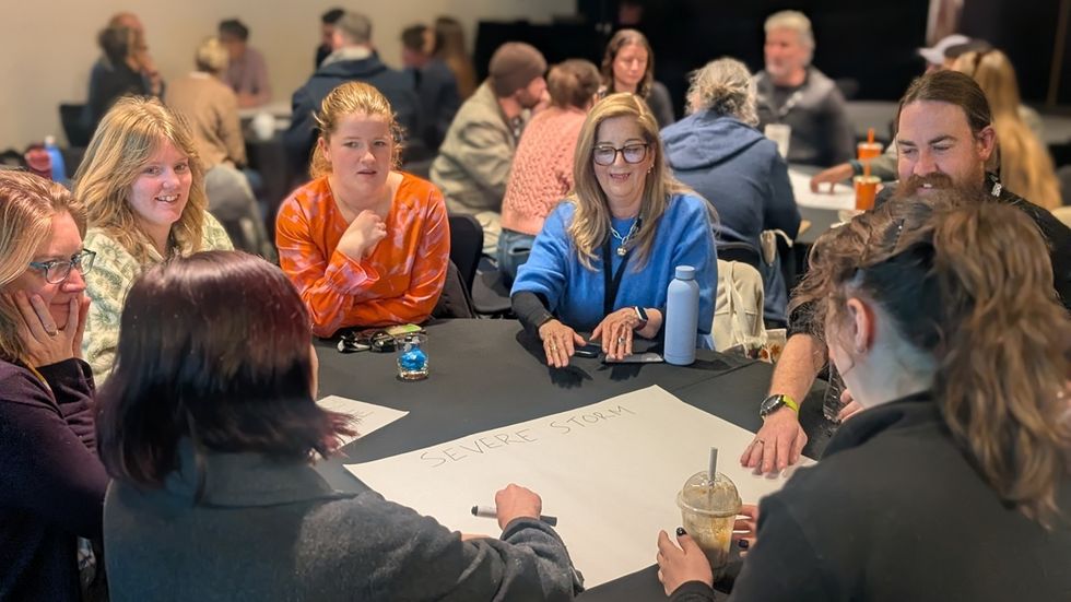Group at the 2026 ZAA conference discussing "Severe Storm" around a table with a large paper.