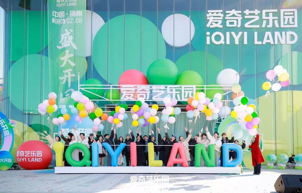 Group celebrating at iQIYI LAND opening with colorful balloons.