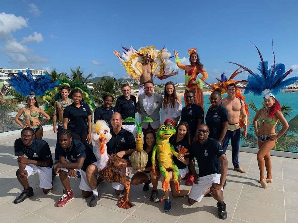 Group in colorful carnival costumes posing by a tropical beachfront.