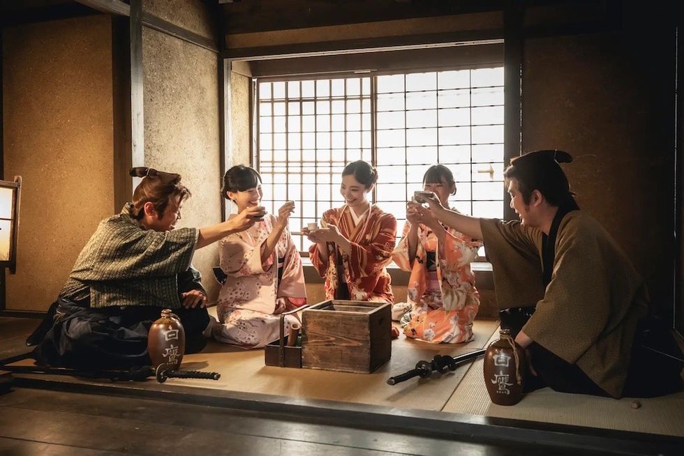 Group in traditional Japanese attire toasting in a tatami room.