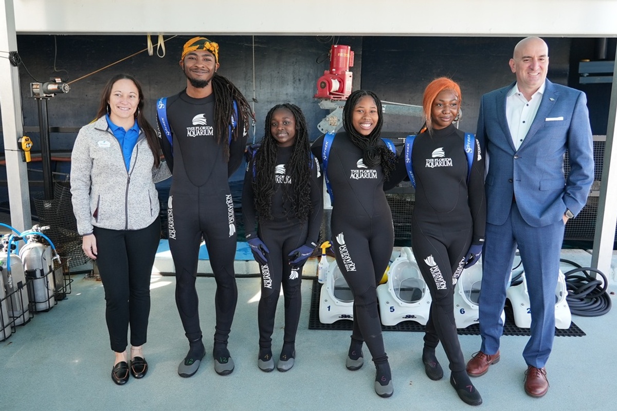 Group in wetsuits poses for a photo at an indoor aquatic facility at the Florida Aquarium's SeaTREK experience