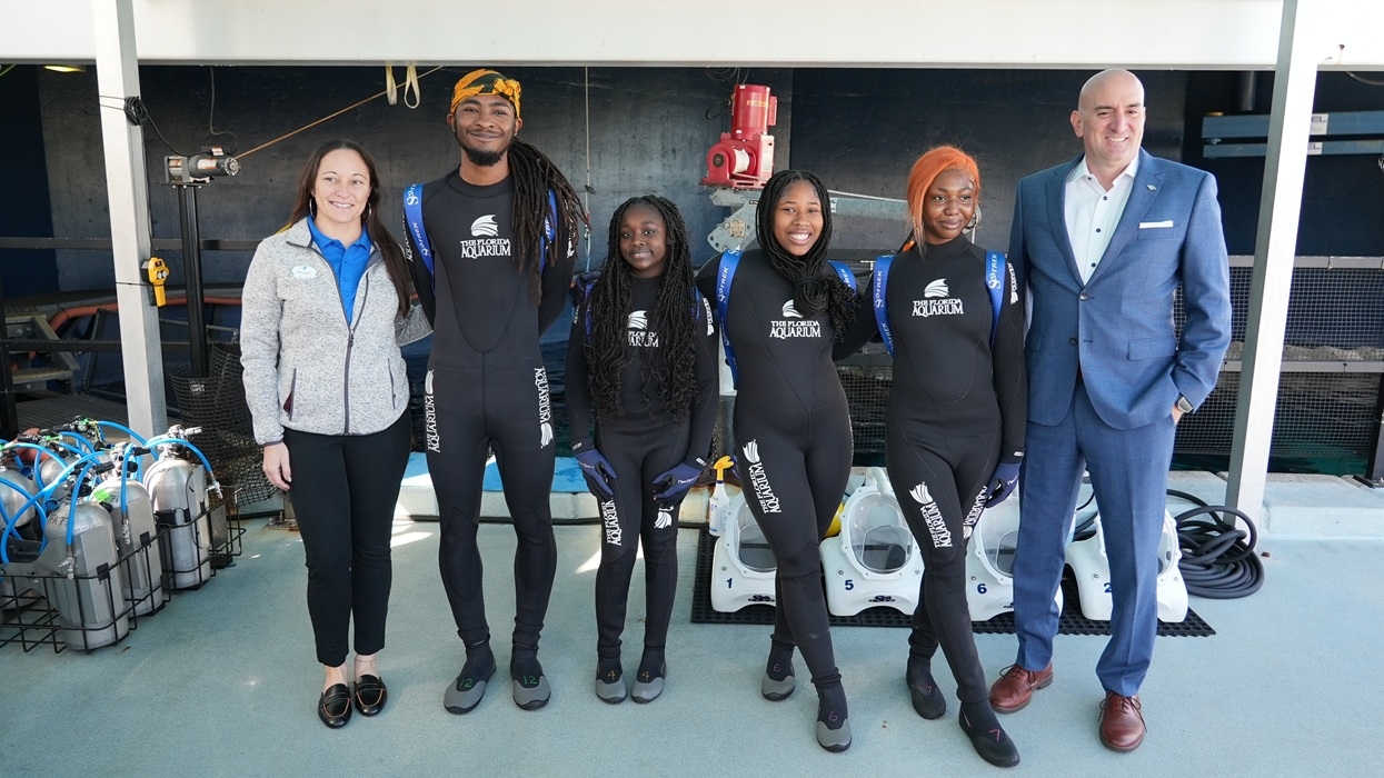 Group in wetsuits poses for a photo at an indoor aquatic facility at the Florida Aquarium's SeaTREK experience