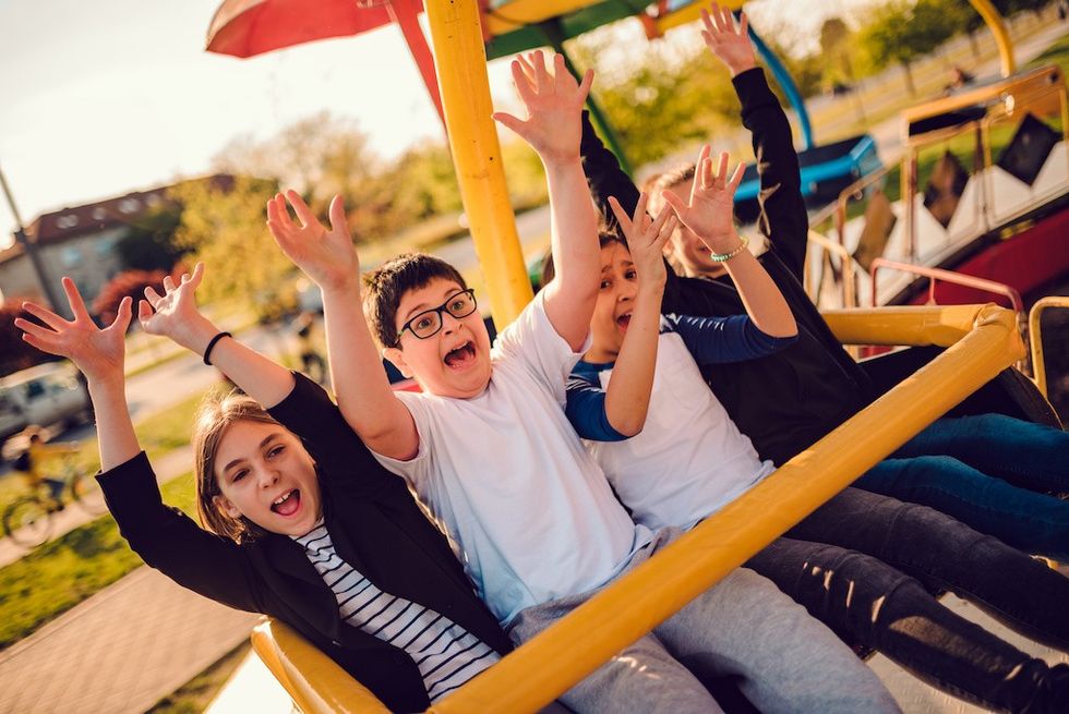 Group of children enjoying on a spinning ride in amusement park with arms raised theme park demographics