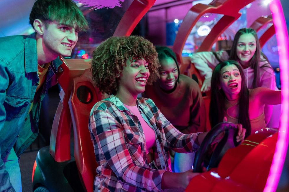 Group of Friends Enjoying a Fun Arcade Racing Game, group of young friends cheer and laugh while playing a racing game at the arcade, fully immersed in the fun and excitement. FECs marketing