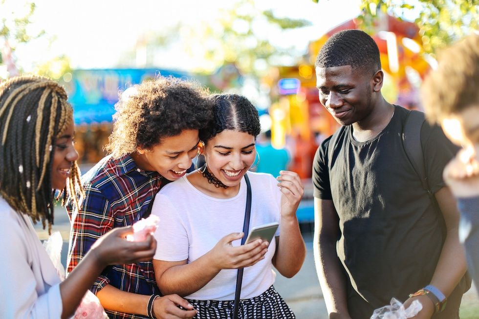 Group of friends laughing while looking at a phone outdoors.