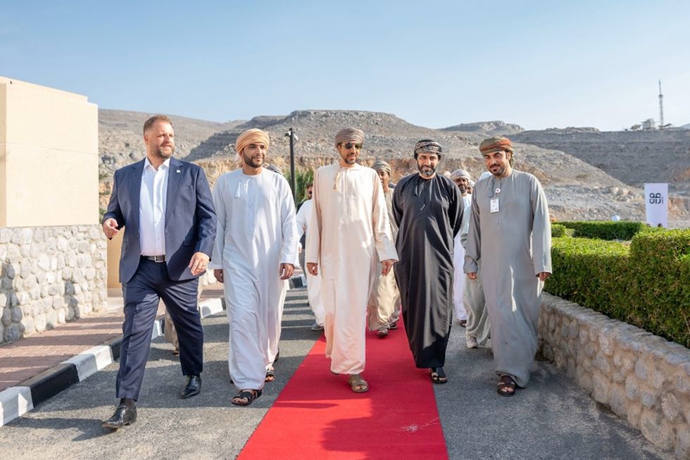 Group of men walking on a red carpet outdoors, with mountains in the background.