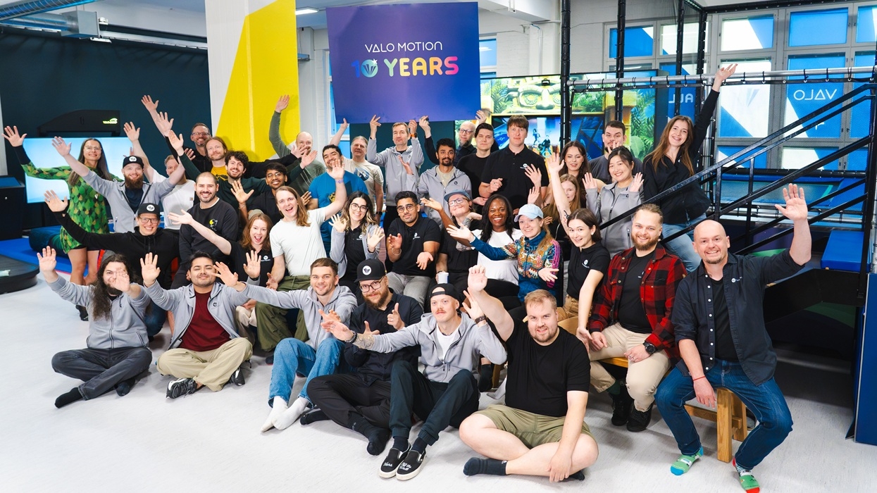 Group of people celebrating "Valo Motion 10 Years," waving and smiling indoors.