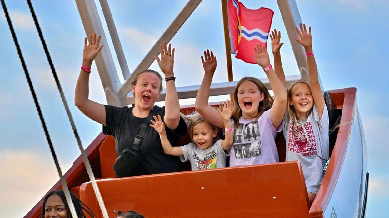 Group of people enjoying a ride, hands up, with a flag waving in the background.