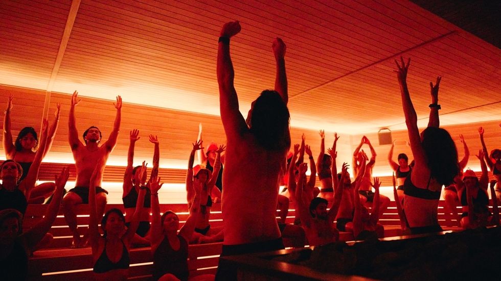 Group of people exercising with raised arms in a warmly lit, wood-paneled room.