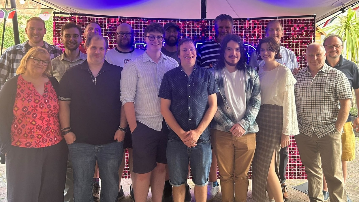 Group of people from Merac smiling, posing under a tent with lights and a colorful backdrop.