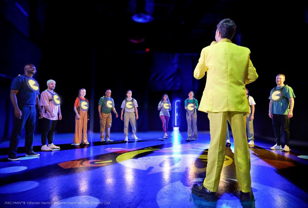 Group of people in a circle, wearing Pac-Man shirts, led by person in yellow suit.