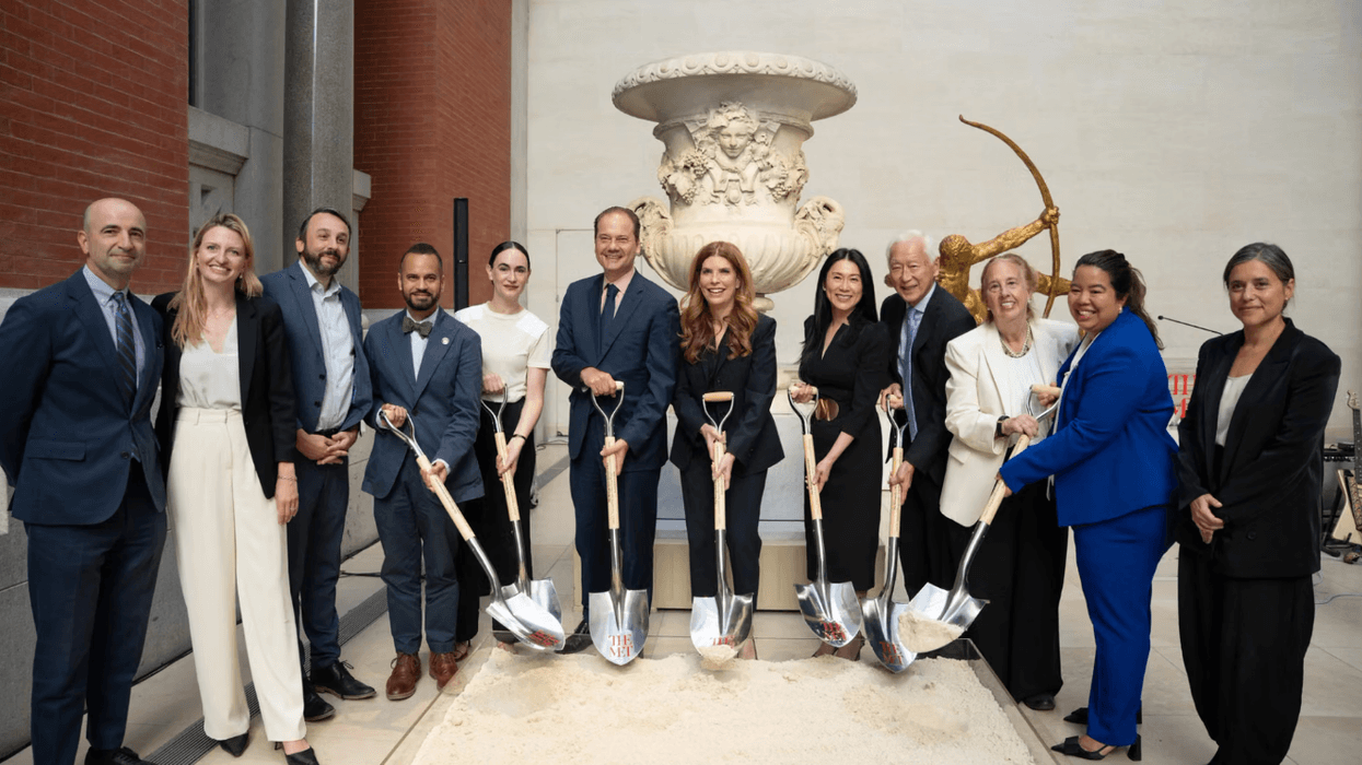 Group of people in formal attire at a groundbreaking ceremony with shovels.