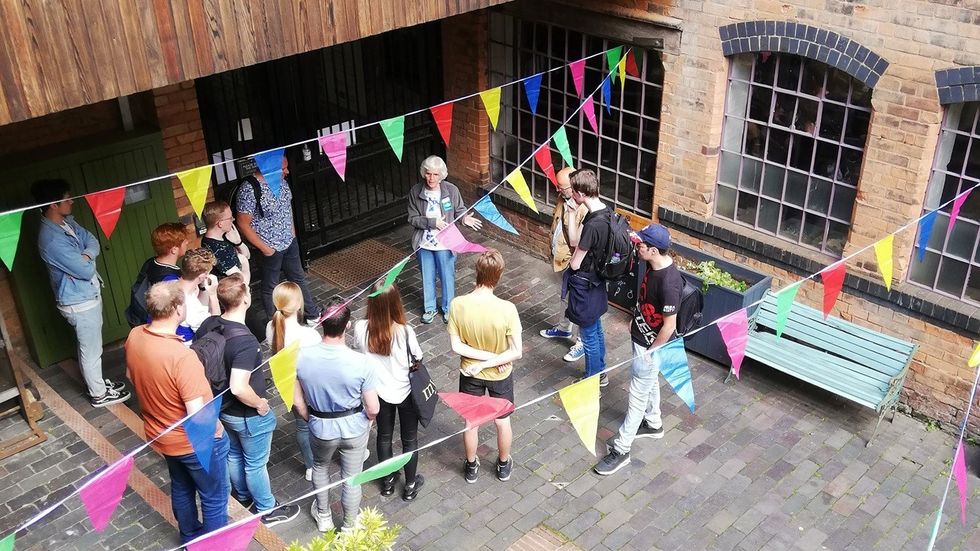 Group of people listening to a speaker outdoors, surrounded by colorful bunting.