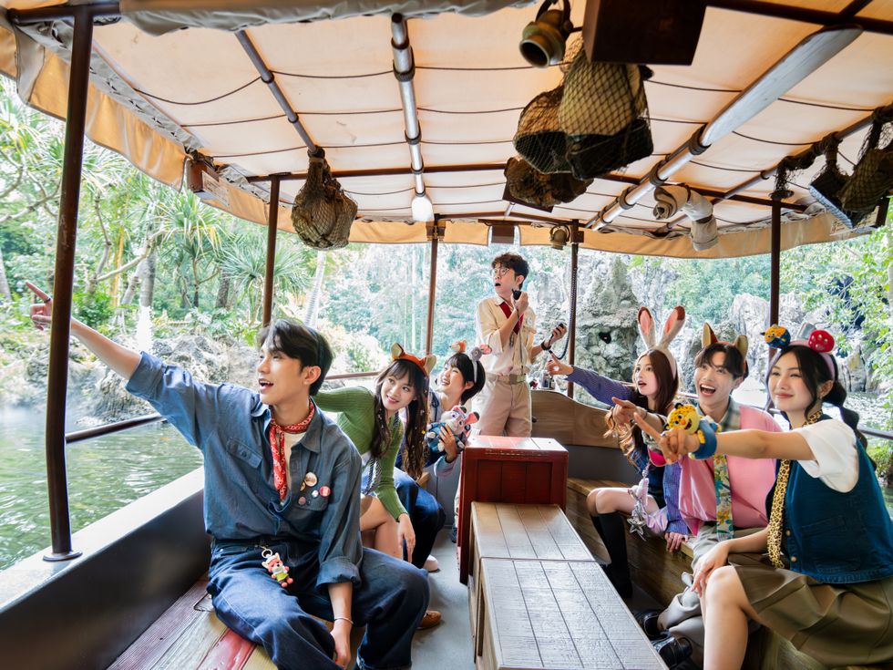 Group of people on a jungle cruise ride, smiling and pointing at surroundings.