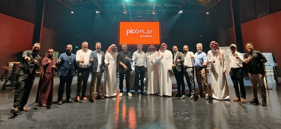 Group of people posing indoors with "pico PLAY" sign in the background.