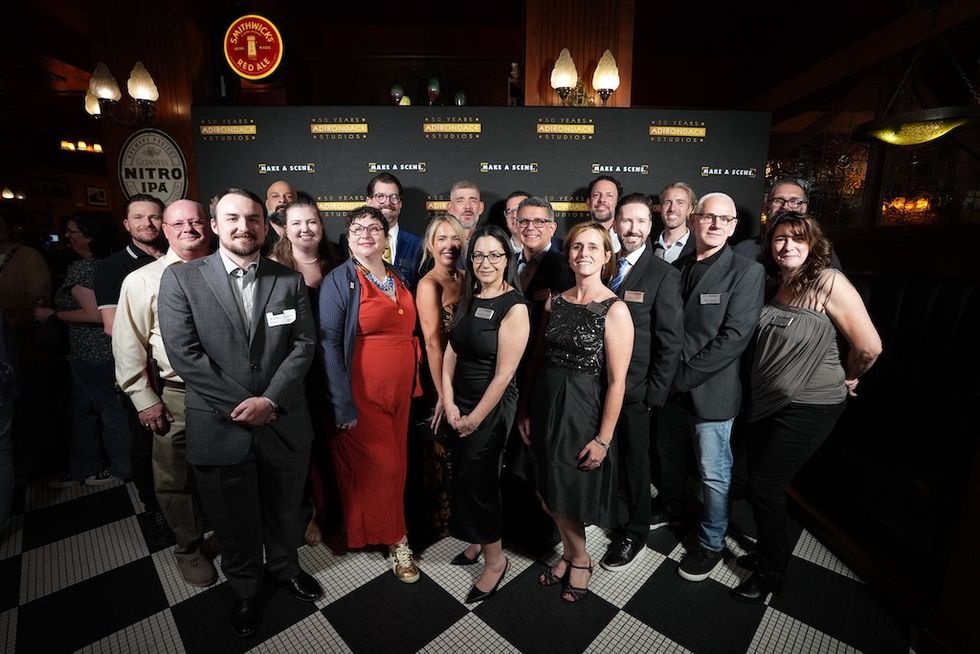Group of people smiling at an event, standing on checkered floor.