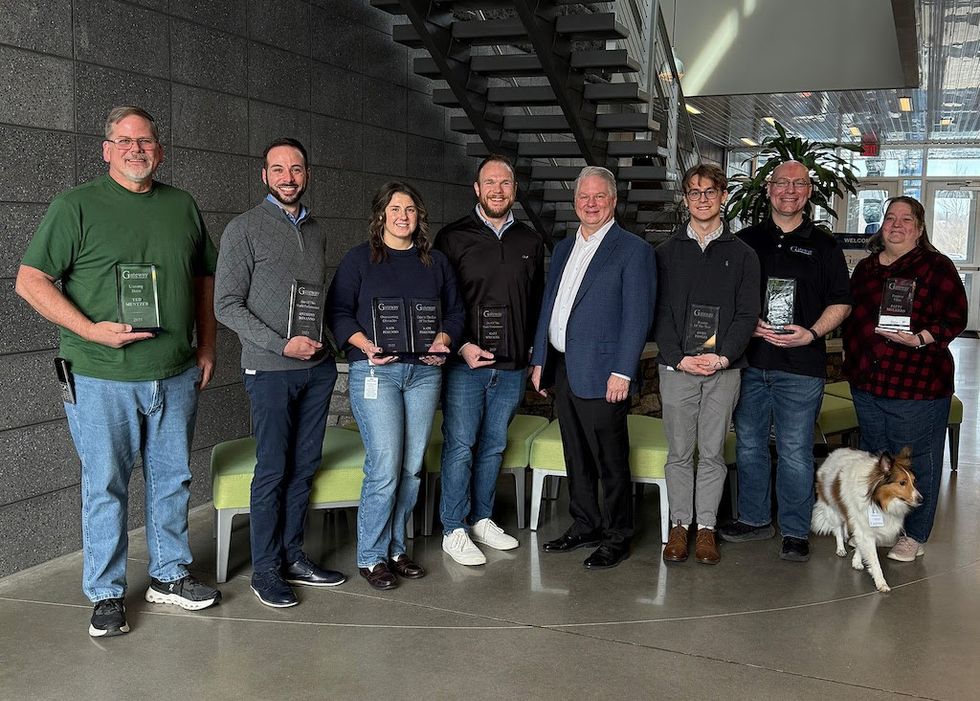 Group of seven people holding awards, posing indoors, one person with a dog.
