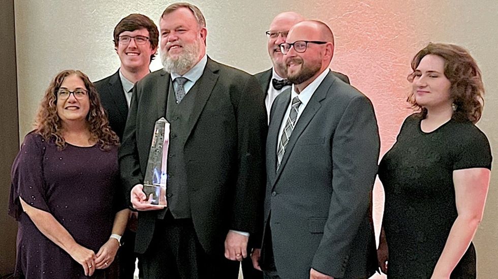 Group of six people dressed formally, one holding an IES Illumination Awards award trophy.