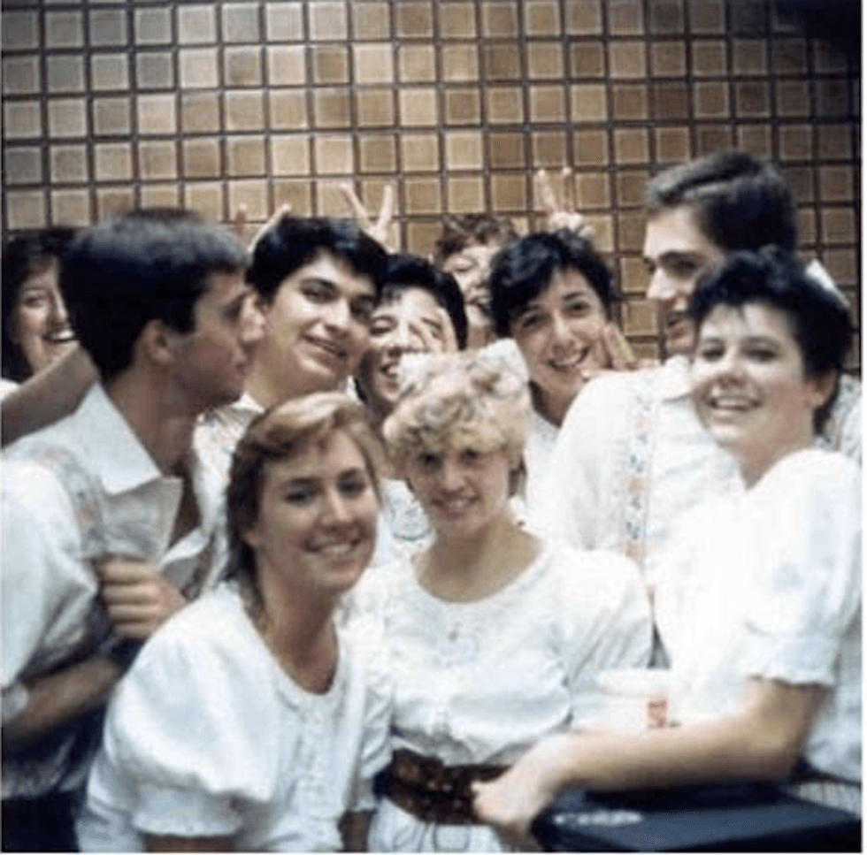 Group of smiling people in white outfits posing indoors with a tiled wall background.