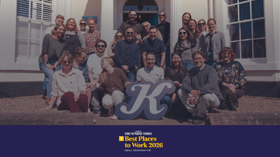 Group of smiling people posing outdoors with a large "Katapult" sign in front of a building, with text reading The Sunday Times Best Places to Work 2026