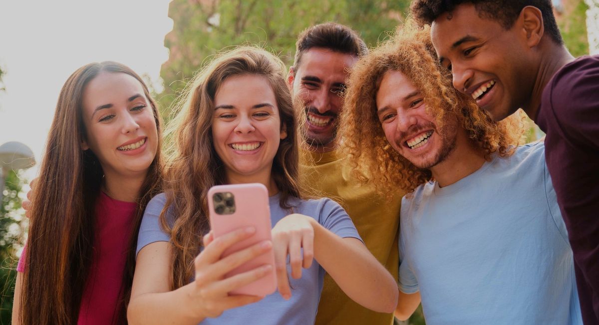 Group of young friends having fun sharing media with a cellphone at street.