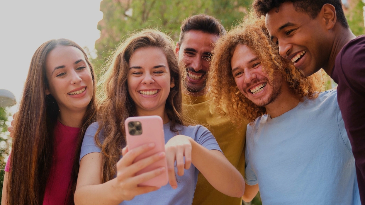 Group of young friends having fun sharing media with a cellphone at street.