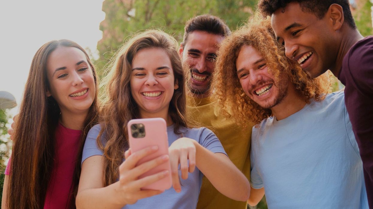 Group of young friends having fun sharing media with a cellphone at street.