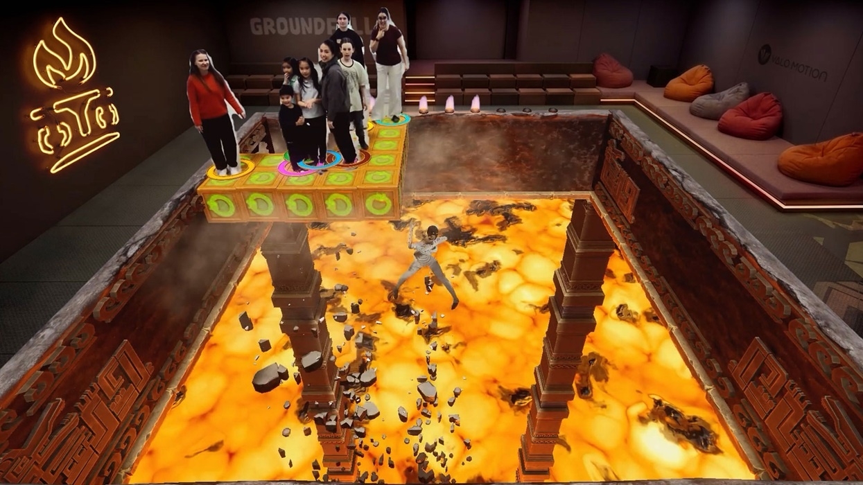 Group on a platform above a virtual lava pit, playing the game 'Groundfall' in an immersive game room setting.