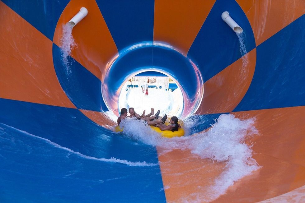 Group on a yellow raft in blue and orange water slide, rushing towards an outdoor pool at Six Flags Hurricane Harbor Phoenix